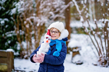 Fototapeta na wymiar Cute little preschool girl with glasses making mini snowman. Adorable healthy happy child playing and having fun with snow, outdoors on cold day. Active leisure with children in winter