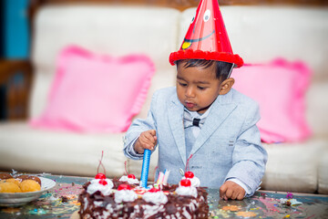 An Asian child in a birthday hat and coat-tie is eating a birthday cake.