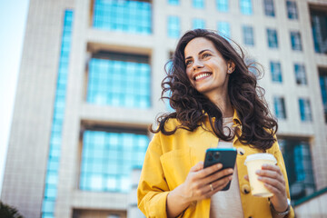 Woman using smartphone and drinking coffee at the city. Closeup shot of a businesswoman using a...