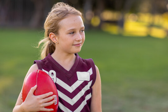 young blonde girl holding red leather football and wearing a football jersey