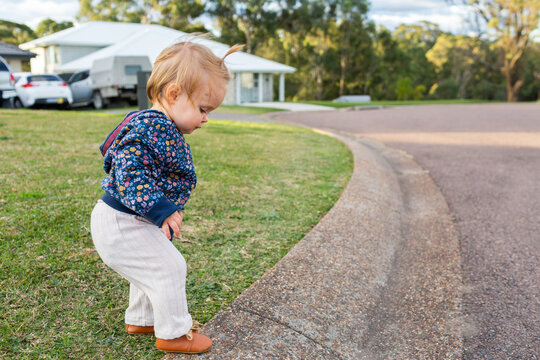 Toddler girl walking along side of road in gutter on urban street
