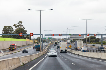 trucks and cars on busy multi lane road in Melbourne, Victoria with variable speed limit signs