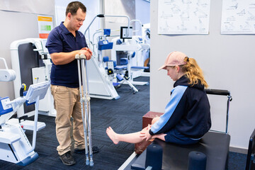 Physiotherapist working with teen girl teaching her how to use crutches  to walk with only one