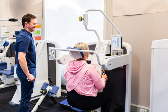 Happy physio standing beside woman using physical therapy equipment