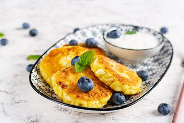 Cottage cheese pancakes with sour cream and blueberries on a light background. Breakfast or lunch.