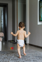 Playful baby running across a living room floor in a diaper. A baby in a diaper running across a...