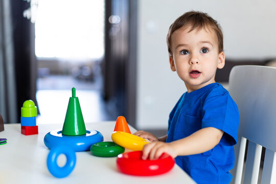 Young Child Engrossed In Imaginative Play At A Table Filled With Toys. A Little Boy Sitting At A Table Playing With Toys