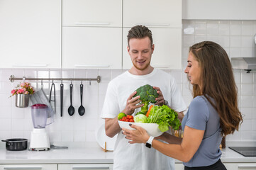 Caucasian young couple in white kitchen cooking making preparing healthy food holding a bowl of mix vegetable.