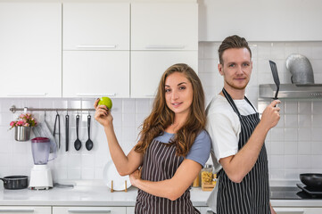 Caucasian young couple in white kitchen cooking making preparing healthy food with vegetables wearing aprons.