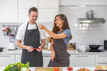 Caucasian young couple in white kitchen cooking making preparing healthy food with vegetables wearing aprons holding a tablet device.