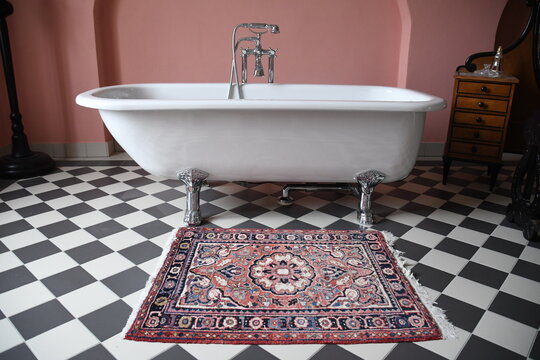 altmodische wei&szlig;e Badewanne mit silbernen Tigerf&uuml;&szlig;en steht auf schwarz-wei&szlig;em Fu&szlig;boden neben Orientteppich