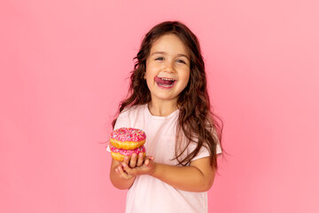 Portrait of a happy little smiling girl with curly hair and two appetizing donuts in her hands on a...