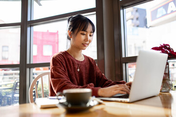 Asian small business owner working remotely on her laptop at a cafe
