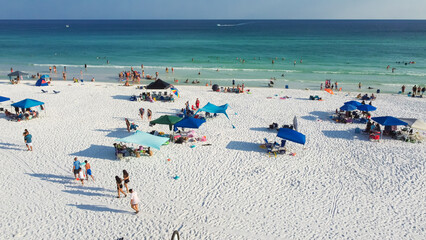 Group of people walking along sugar-white sandy beaches next to crowed colorful umbrella along turquoise water, gorgeous shade blue waves in Miramar beach, South Walton, Florida, USA