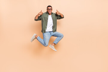 Fototapeta na wymiar Full length portrait of excited man jumping hands fingers demonstrate thumb up empty space isolated on beige color background