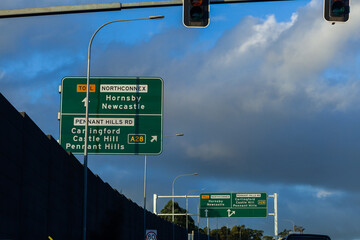 Green signs above road with arrows and directions to pennant hills A28