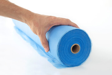 A hand unwinds a roll of blue fabric, a sheet for massage, on a white background.