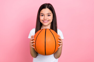 Photo portrait of adorable schoolkid female holding basketball ball sport lesson wear trendy white outfit isolated on pink color background