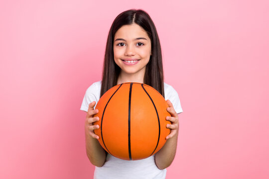 Photo portrait of adorable schoolkid female holding basketball ball sport lesson wear trendy white outfit isolated on pink color background