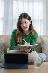 Naklejka premium Asian Hispanic student wearing headphones talking in online chat meeting using tablet computer at bloom distance learning female college student vertical image