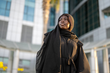 Fototapeta na wymiar Low angle view of beautiful muslim woman wearing traditional Abaya dress on city street.