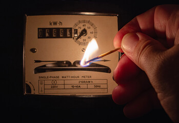Men's hand in complete darkness holds a burning matchstick to reading a home electric meter or...
