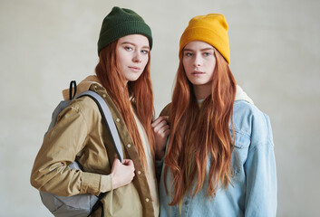 Medium studio portrait of two red-haired young Caucasian women wearing stylish casual clothes and backpacks looking at camera