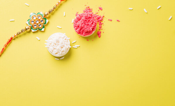 Raksha Bandhan, Indian festival with beautiful Rakhi and Rice Grains on yellow background. A traditional Indian wrist band which is a symbol of love between Sisters and Brothers
