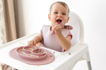 happy baby sits in a highchair and eats complementary foods on white background
