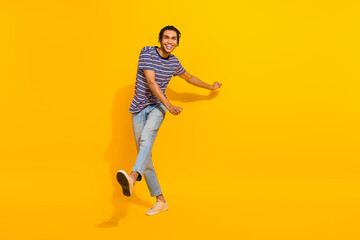 Fototapeta na wymiar Full size photo of pleasant funky good mood man wear stripped t-shirt denim trousers go shopping isolated on yellow color background