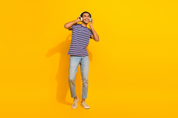 Full length photo of satisfied guy dressed stylish t-shirt jeans hands on headphones enjoy playlist isolated on yellow color background