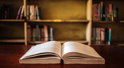 On a wooden table, there's an open book with a library visible in the background. A stack of books nearby adds to the theme of educational learning.