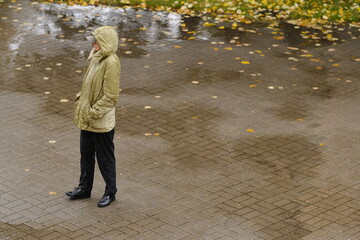 a woman in a pink jacket in black shoes and green trousers with a red bag in her hands walks down...