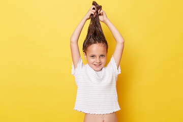 Funny little girl with wet hair wearing casual white T-shirt standing isolated over yellow...