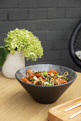 A bowl of udon noodles, veal and fried vegetables angle view on wooden table