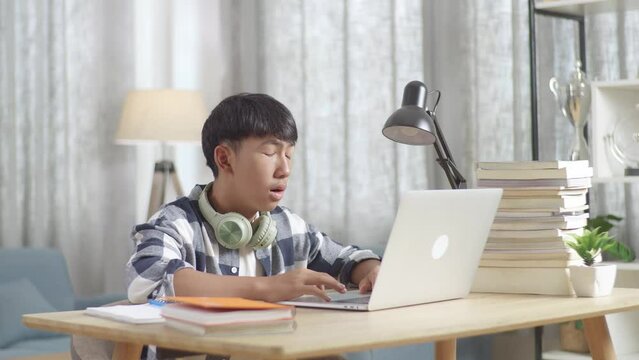 Bored Asian Teenager Yawning While Doing Home Work On Laptop, Student Learning Online At Home
