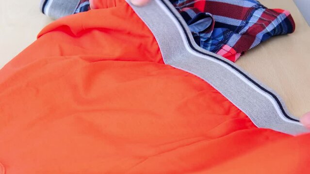 bright orange, checkered men's cotton boxer shorts close-up, female hands testing, choice of underwear in store, checking elastic band, Choosing Fashionable Cotton Boxers in Store