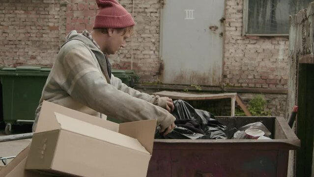 Tilt down shot of homeless man rummaging in trash cans looking for clothes on street
