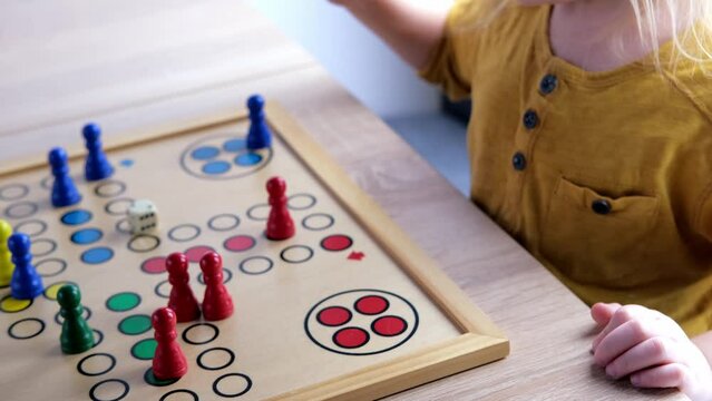 close-up hands of small child manipulate with wooden figurines of family board game, smart kid, 2-year-old girl is learning to count, Cross and circle game Parcheesi, foreground focus