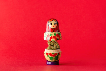A wooden matryoshka doll stands on a red background, in it is a dry bud of medical marijuana.  Alternative treatment with medical cannabis