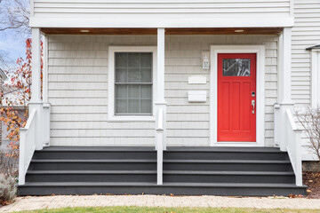 Detail of a front porch of a white home with grey steps leading up to a red door.