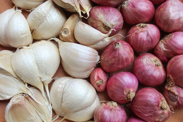 Garlic cloves and red onion or shallots on wooden plate, isolated on white background