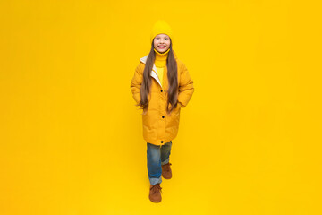 A little girl in full height in an autumn coat, down jackets and hats, rejoices in autumn. Autumn clothes for children. Yellow isolated background.