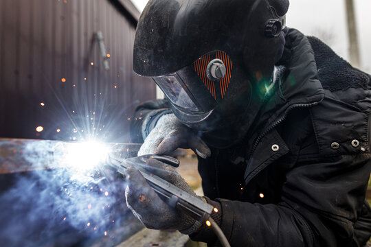 Welder man welding metal iron with electrodes, worker wearing protective helmet and gloves. Close up of electrode welding and electric sparks. Shielded metal arc welding