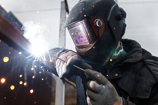 Shielded metal arc welding. Worker welding metal with electrodes, wearing protective helmet and gloves. Close up of electrode welding and electric sparks