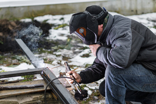 Welder man welding metal iron with electrodes, worker wearing protective helmet and gloves. Close up of electrode welding and electric sparks. Shielded metal arc welding