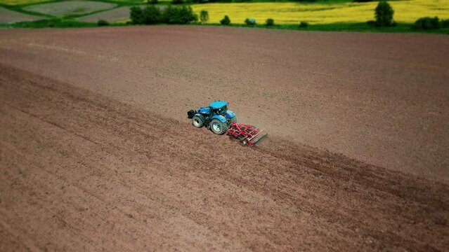 Agricultural tractor plowing a field before sowing grain. Farm machinery with a harrow plows the land in a cultivated agricultural field. Aerial view. 4k footage
