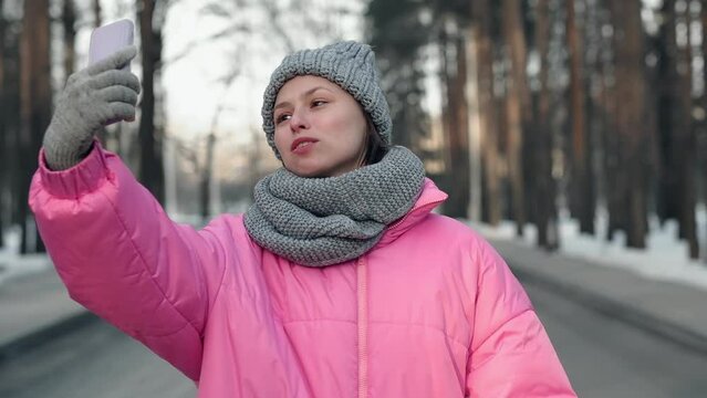 Pretty young girl blogger in a pink jacket is taking selfie in winter