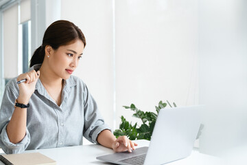 Concentrated young beautiful businesswoman working on laptop in bright modern office