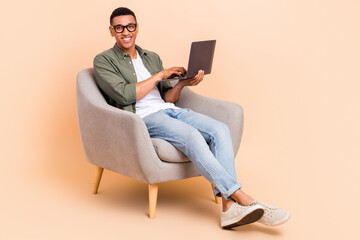 Full body photo of cheerful friendly person sitting comfy chair use wireless netbook isolated on beige color background